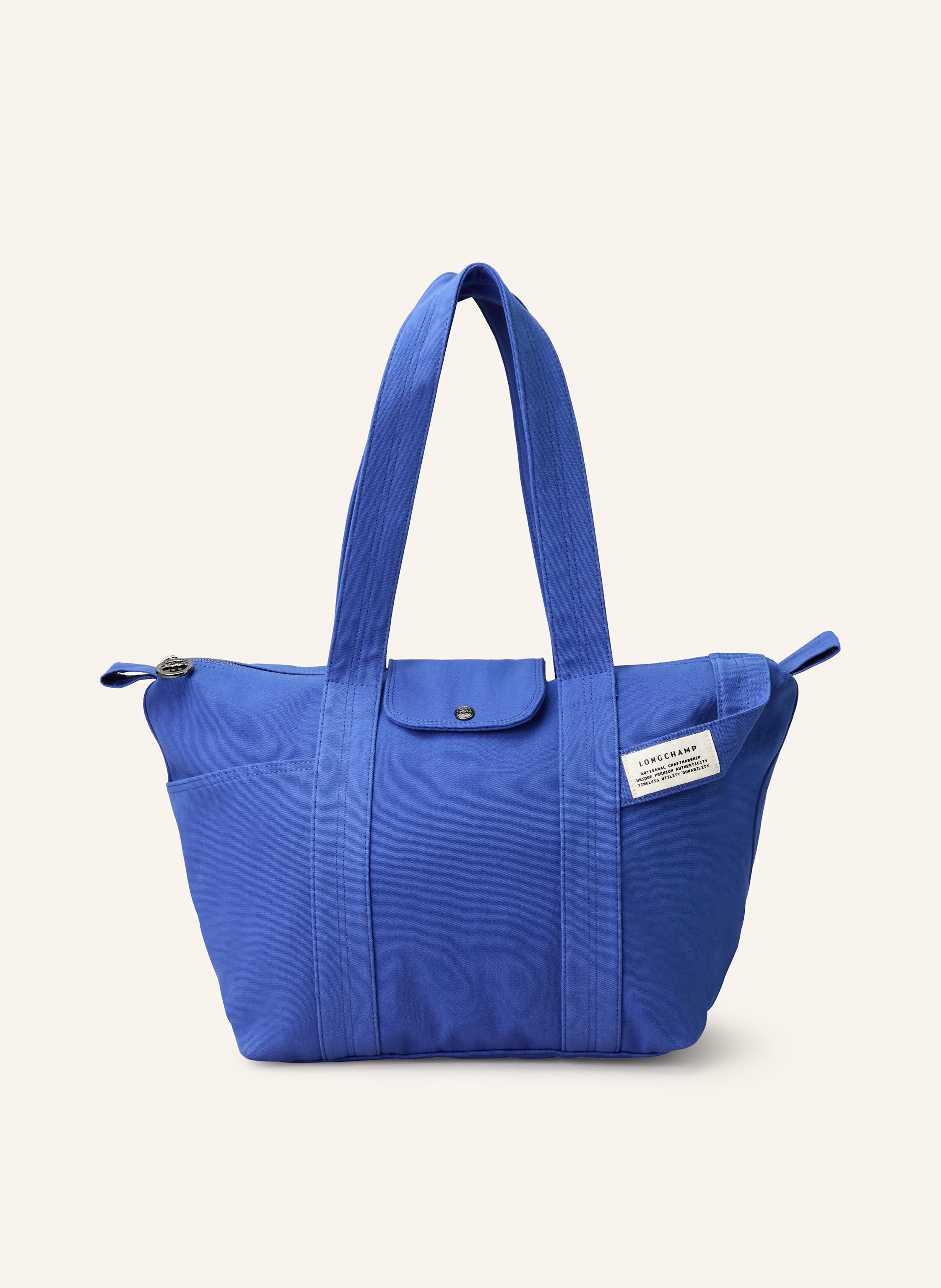 Longchamp Canvas. Schließt mit Reißverschluss und Druckknopf. Zwei Tragegriffe. Außenfach auf der Vorderseite. Innen ein Hauptfach. Ein Steckfach für Smartphone & Co. Dekorative Schlaufe mit Label-Badge auf der in blau