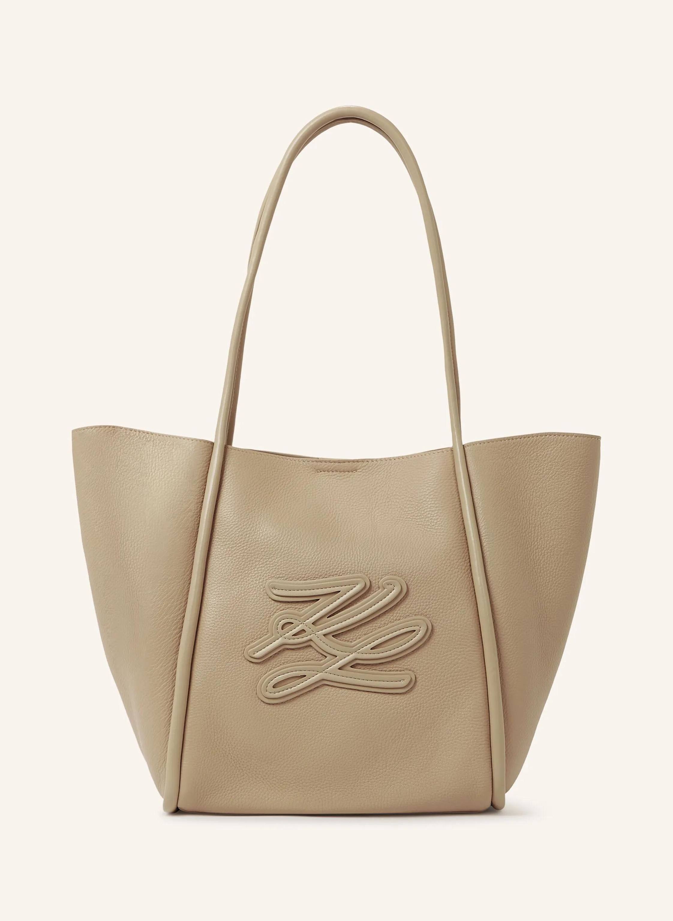 Karl Lagerfeld This medium tote bag blends a spacious, laptop-friendly silhouette with elongated twin handles for effortless carrying. The tonal Karl Autograph logo adds a refined, modern touch. Perfect from office in beige