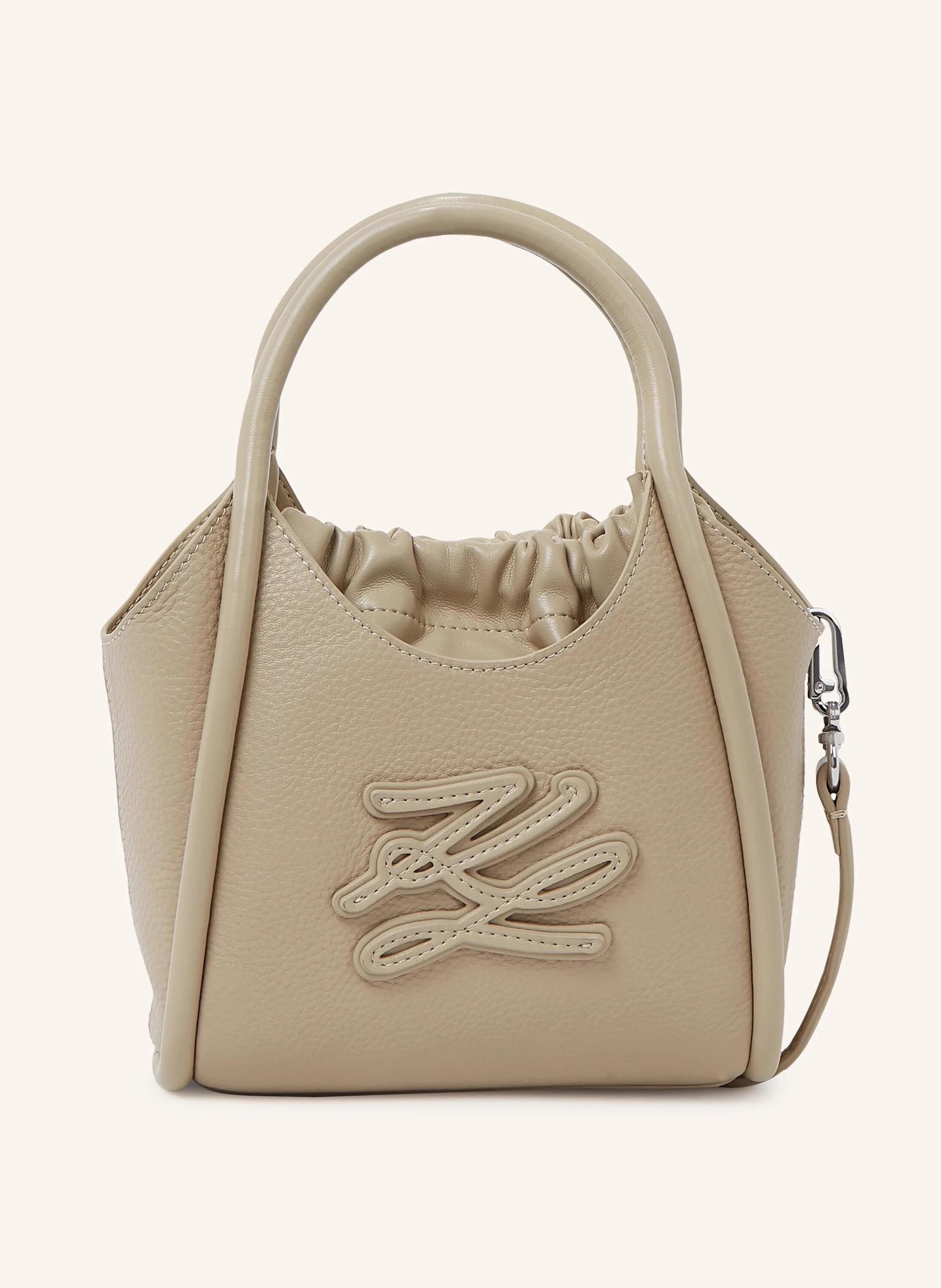 Karl Lagerfeld The K/Autograph mini tote bag blends elegant design with practical versatility. Its supple cow leather and tonal logo create a refined look, while the interior drawstring pouch and adjustable strap ke in beige